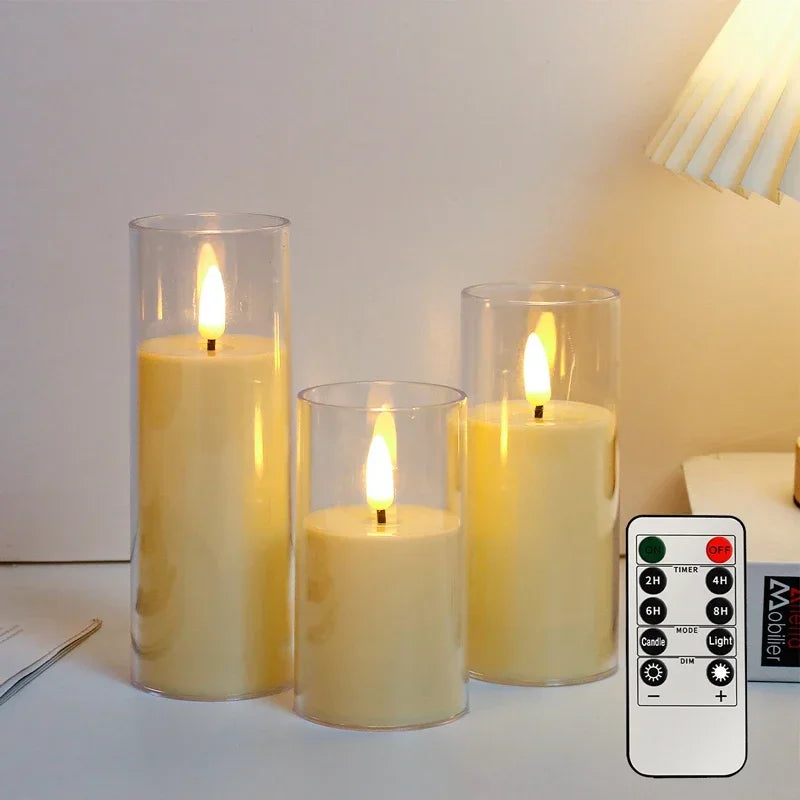 Set of three flameless candles in glass holders with a remote control on a table.