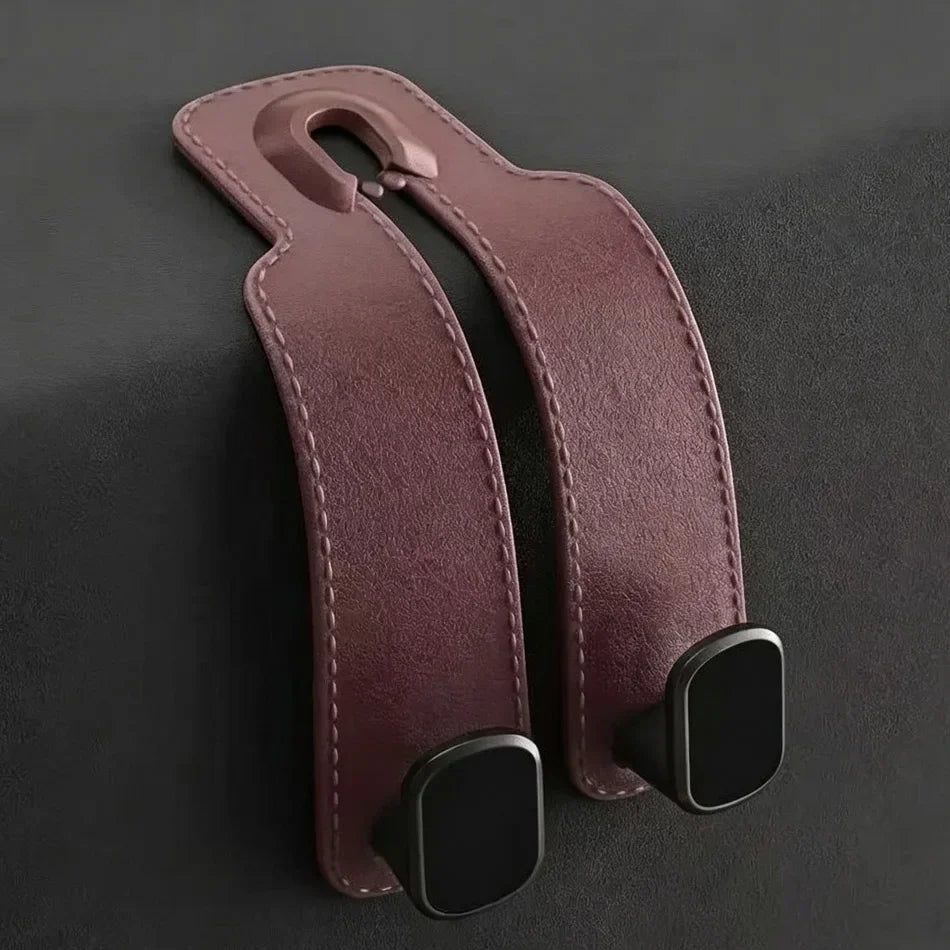 A pair of dark brown faux-leather strap covers with black plastic snap hooks, shown on a dark gray textured background.