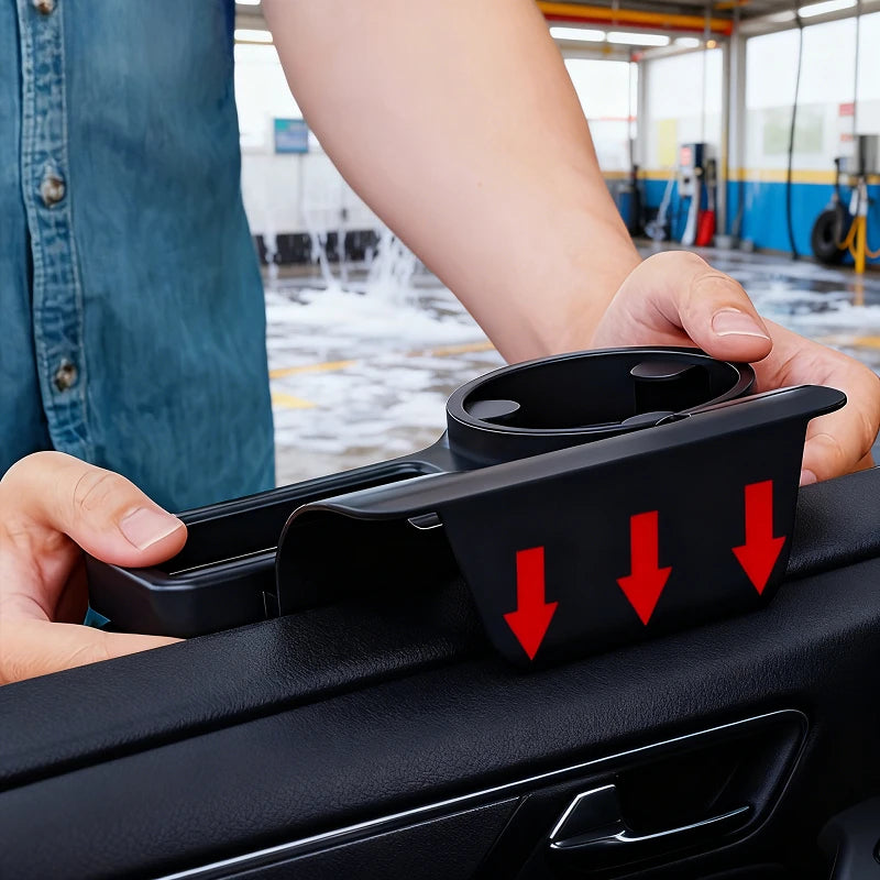 A person holds a black car door pocket organizer with a cup holder insert in a car wash setting. Red arrows on the product indicate the downward pressing action.