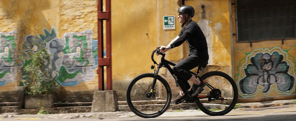 A person riding a black mountain bike along a street next to a yellow wall with graffiti murals.