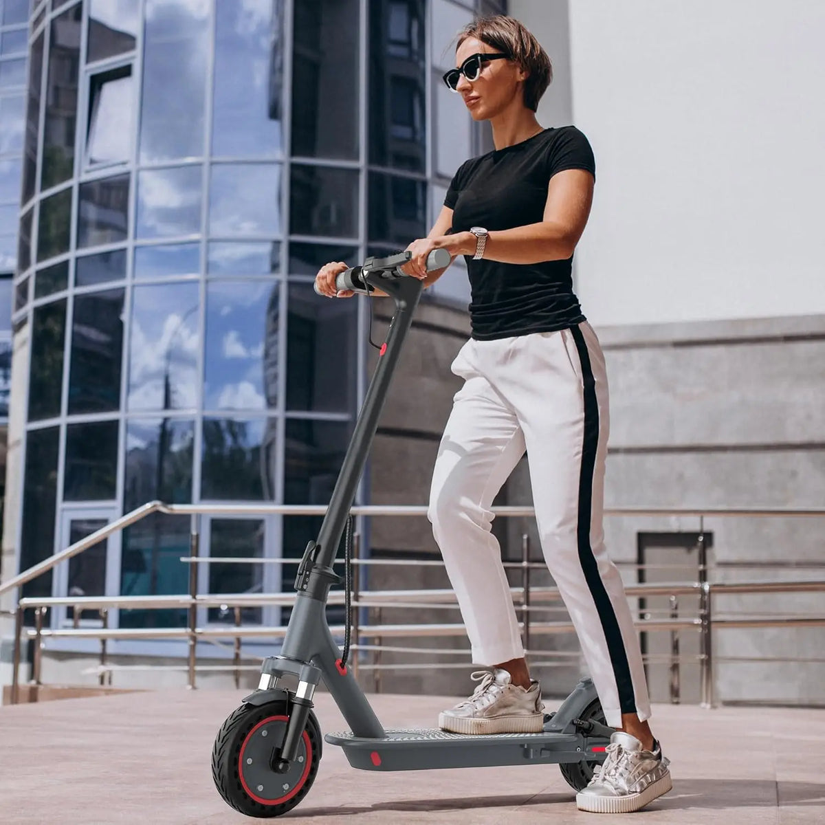 Woman riding a gray electric scooter outdoors in an urban setting.
