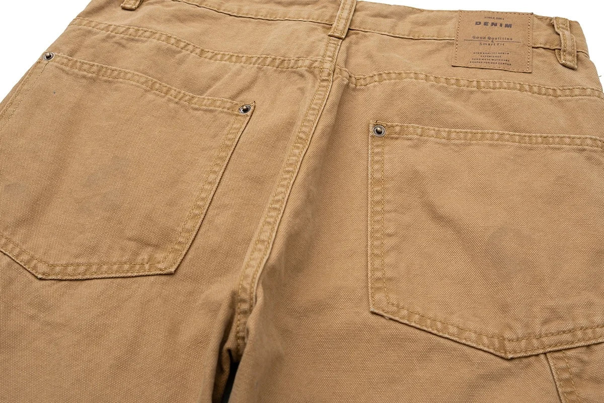 Close-up of the back of tan canvas pants showing two rear patch pockets, belt loops, and a leather brand label at the waistband.