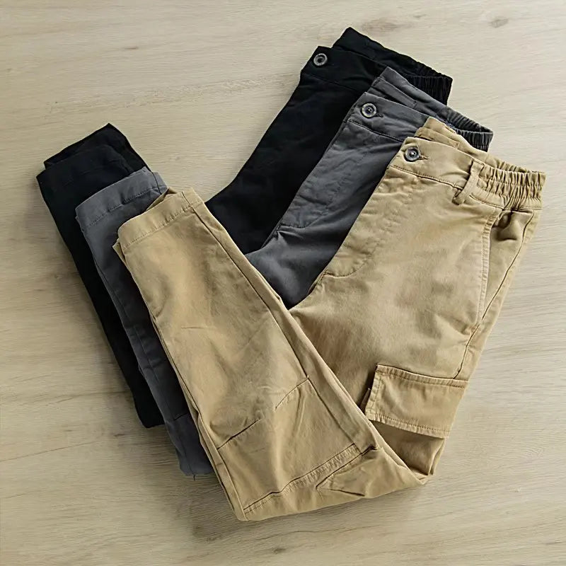 Three pairs of pants in black, gray, and beige on a light wooden surface