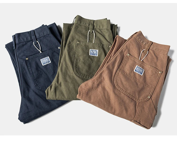 Three pairs of folded corduroy pants in navy blue, olive green, and brown, arranged diagonally on a light gray background.
