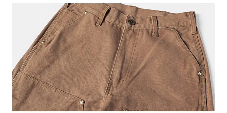 Close-up of brown corduroy trousers showing the waistband, belt loops, button closure, and front pocket details against a light gray background.
