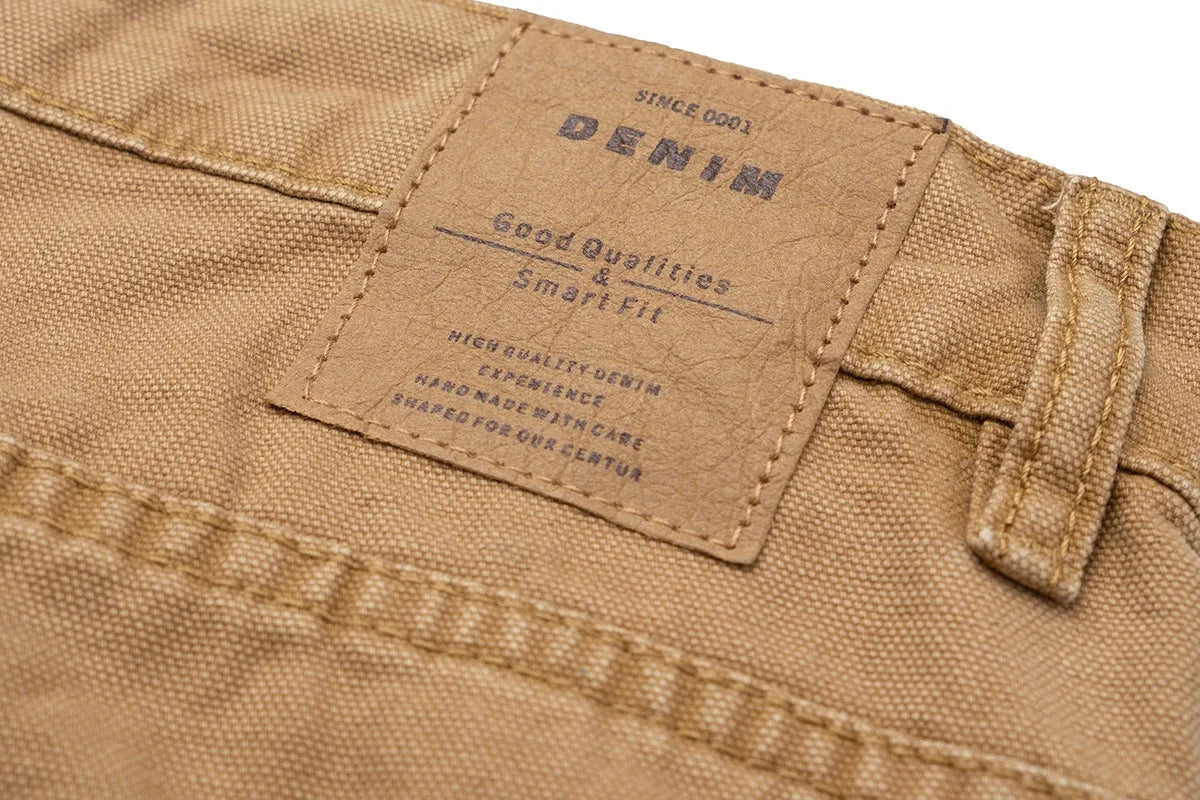 Close-up of a tan denim fabric product showing a stitched label that reads 'DENIM' with smaller text including 'SINCE 1903' and 'Good Quality & Smart Fit'.
