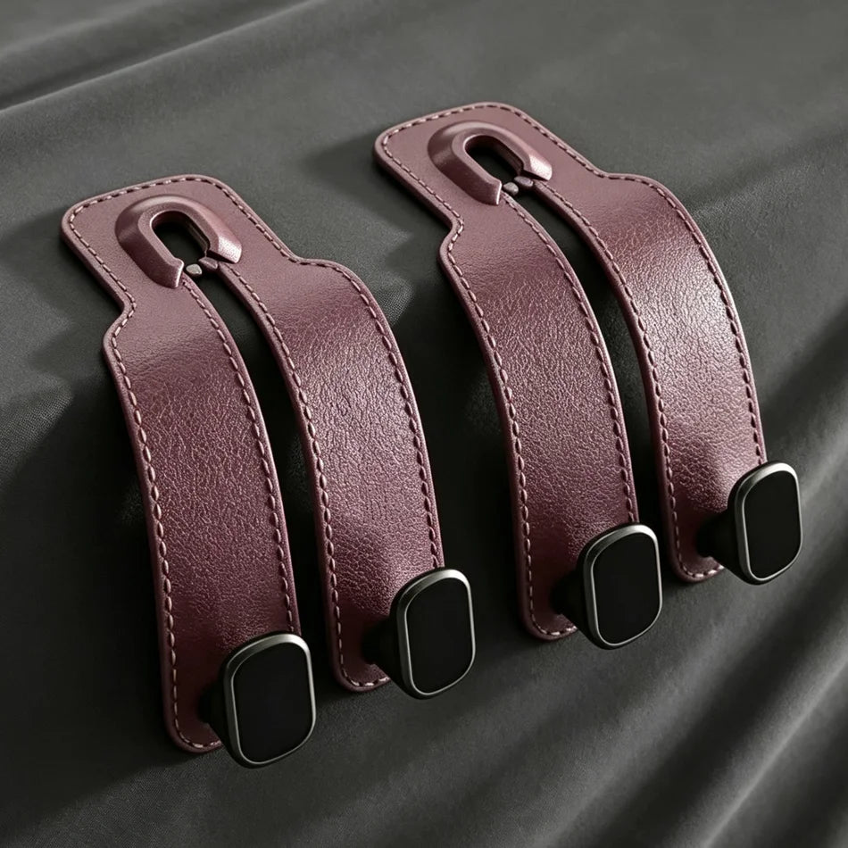 Two burgundy leather strap-like accessories with stitched edges and black rectangular end pieces, arranged on a dark gray fabric background.