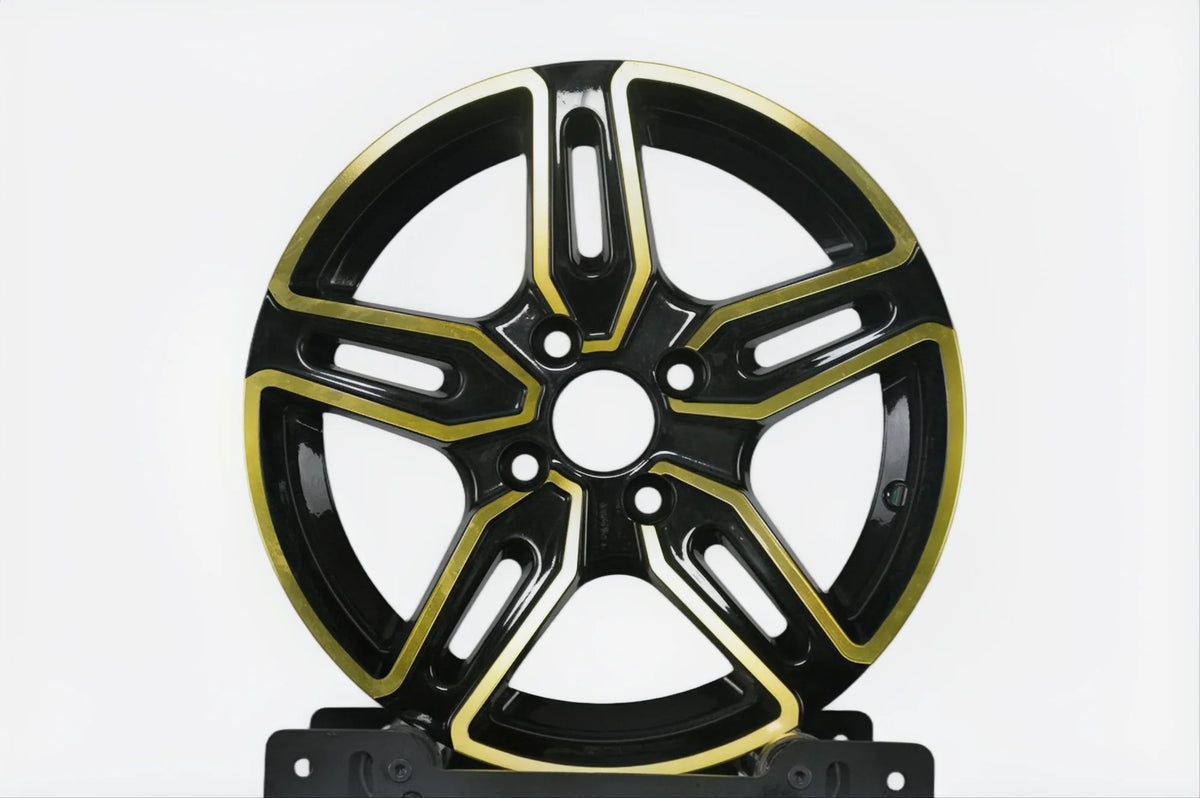 A multi-spoke alloy wheel rim in glossy black with polished gold accents, displayed on a black stand against a light gray background.