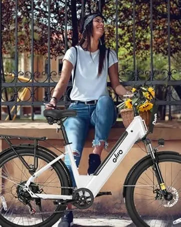 A woman sits on a white electric bicycle with a basket of sunflowers, parked outdoors in front of a black metal fence. The bike frame has the brand name 'aliro' printed on it.