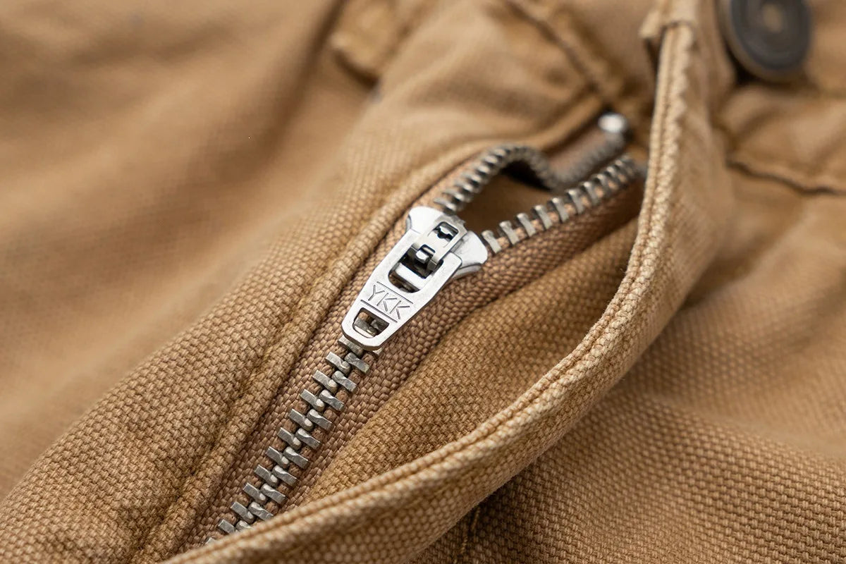 Close-up of a tan canvas jacket with a silver metal zipper and a visible Kipsta logo on the zipper pull.