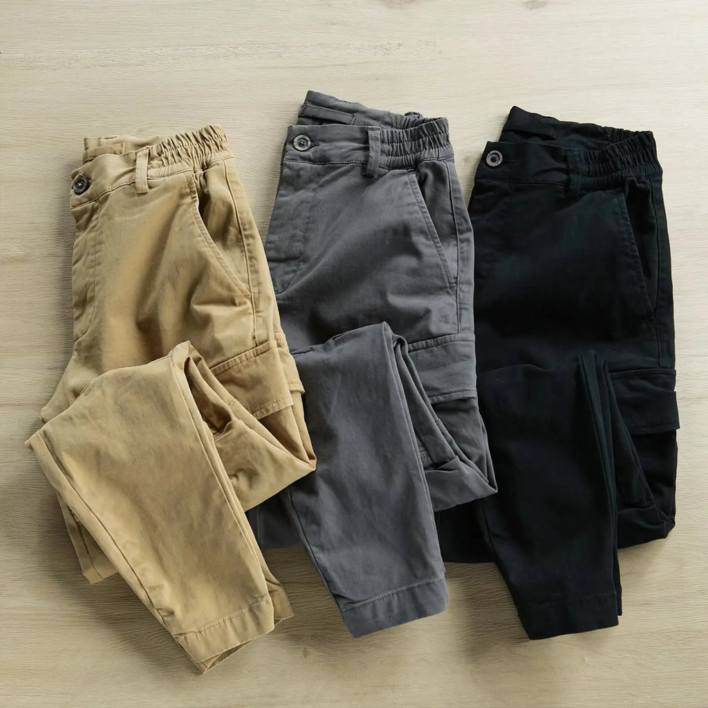 Three pairs of pants in beige, gray, and black on a light wooden surface.