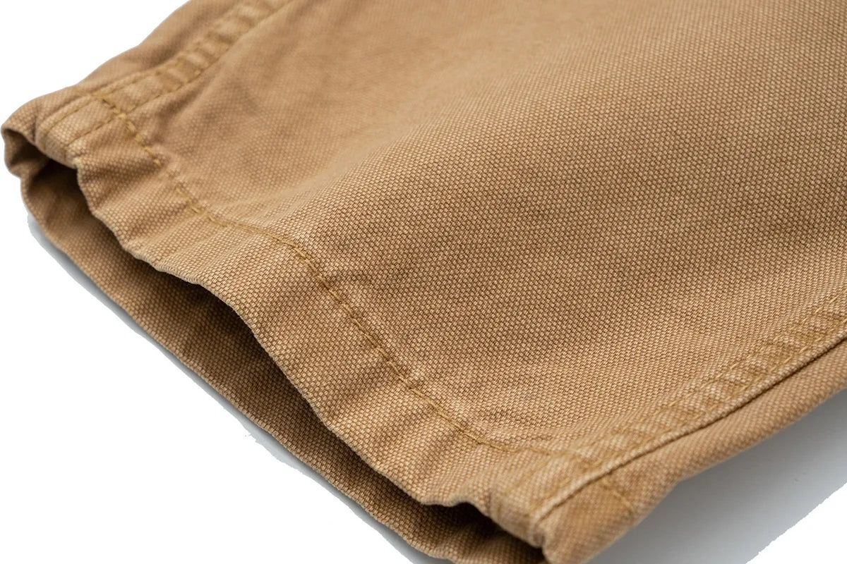 Close-up of folded tan canvas fabric with visible weave texture and stitched edge on a white background.