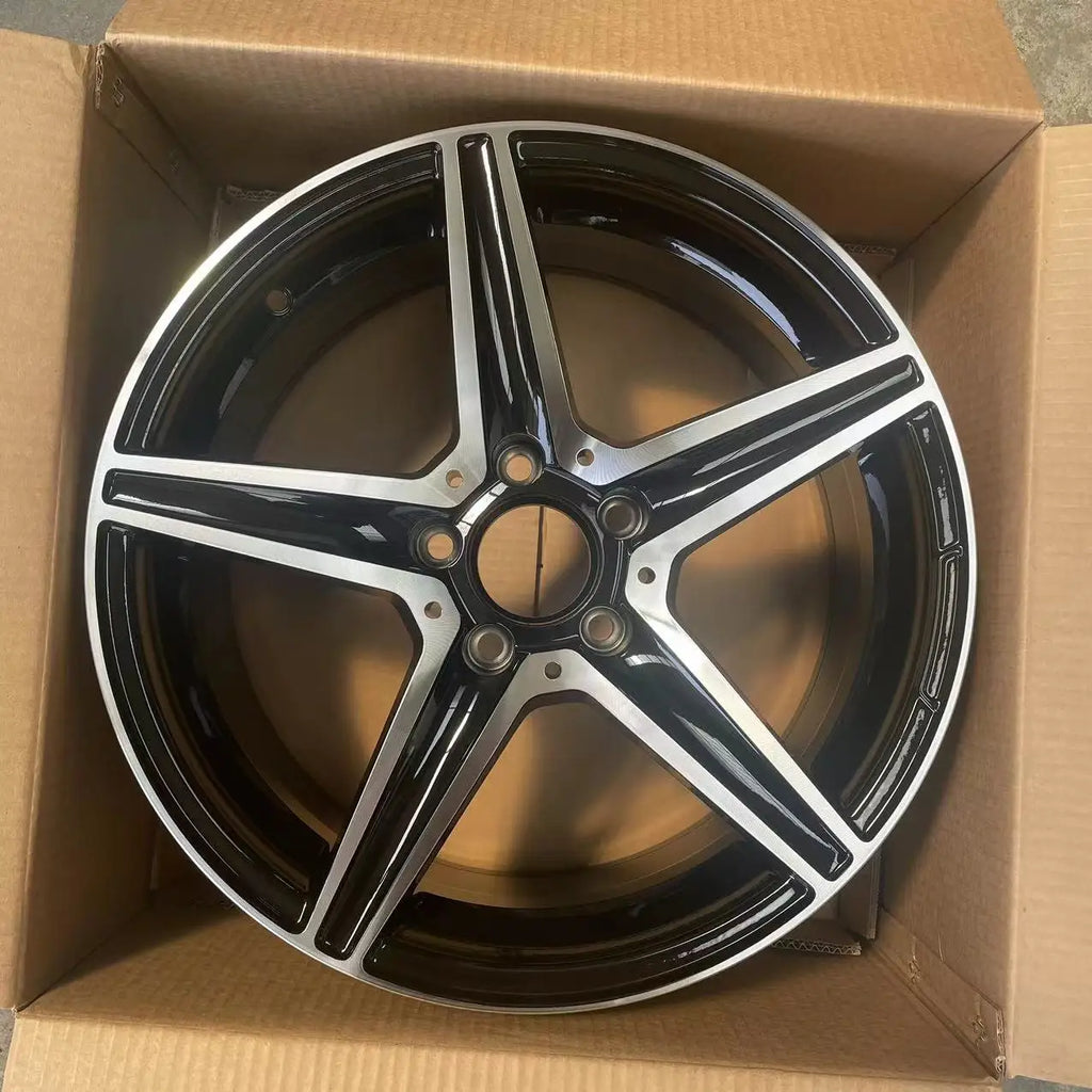 A glossy black and silver multi-spoke alloy wheel rim, shown inside an open brown cardboard box.