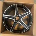 A glossy black and silver multi-spoke alloy wheel rim, shown inside an open brown cardboard box.
