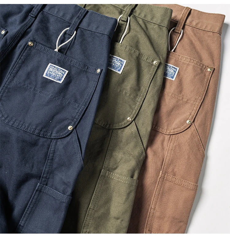 Three pairs of work pants in navy blue, olive green, and brown, arranged diagonally to show the front pockets and waistband details of each colorway.