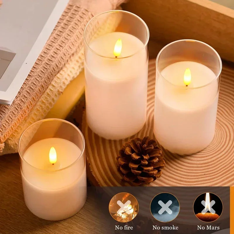 Three lit candles in glass holders on a wooden surface with a pine cone.