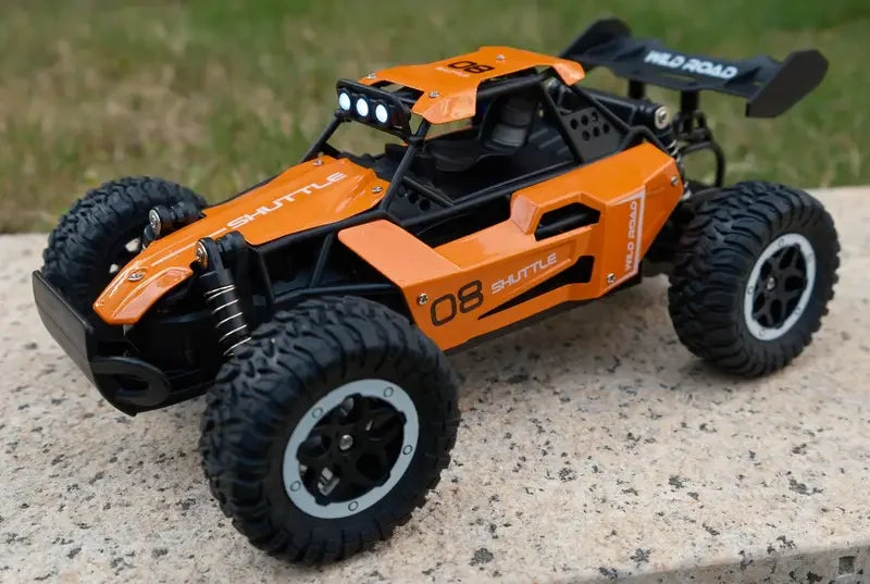 Orange remote control car on a concrete surface with grass in the background