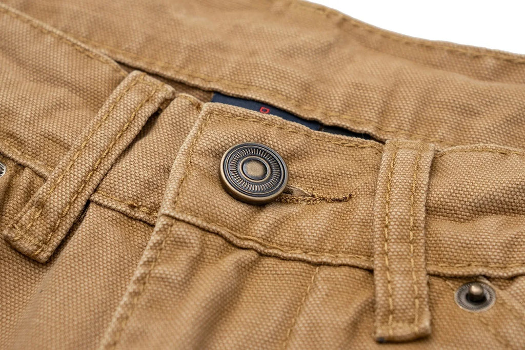 Close-up of tan canvas pants showing the waistband, belt loops, button closure, and detailed fabric texture.