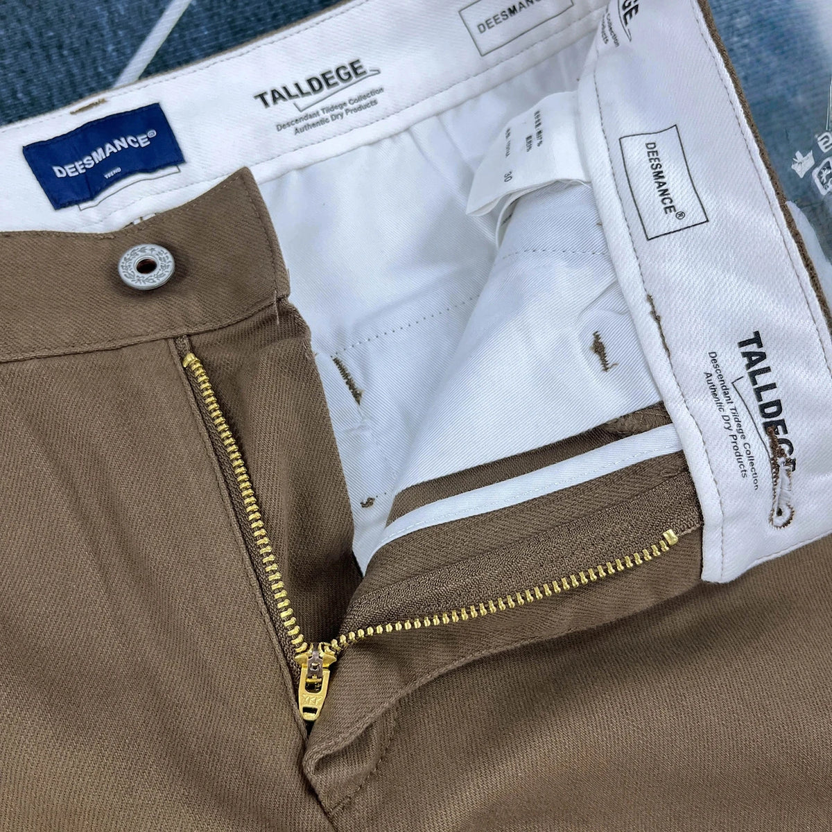 Close-up of a pair of brown chino pants showing the inner waistband, white lining, zipper, and Dreesmann brand labels.
