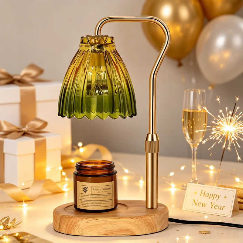 A festive New Year table setting featuring a green ribbed glass table lamp with a gold metal stand and a wooden base, alongside an amber glass jar candle. The scene is decorated with gold and white balloons, a champagne flute, a lit sparkler, wrapped gift boxes, and a 'Happy New Year' card on a warm, softly lit background.