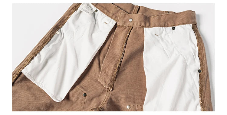 Close-up of a pair of brown and white color-blocked pants, showing the waistband, button details, and textured fabric panels.