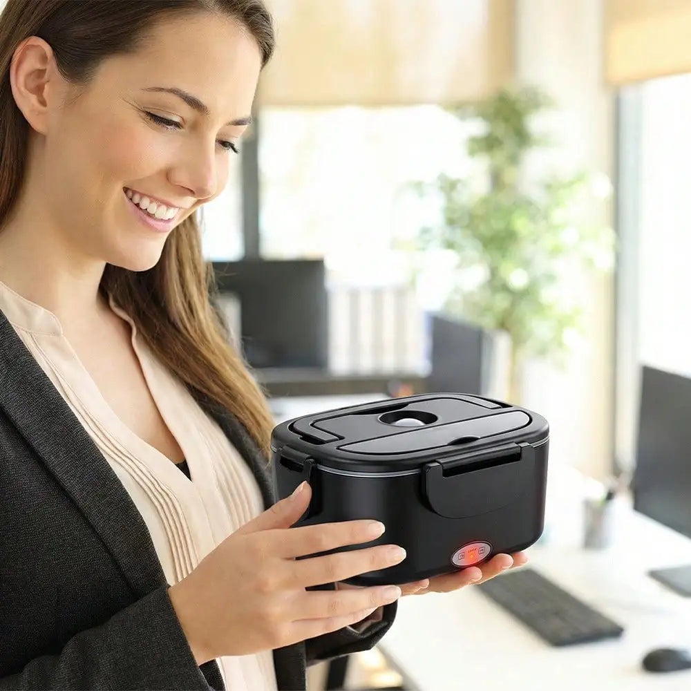 A woman in a gray blazer and beige top holds a black insulated lunch container with a lid in an office setting.