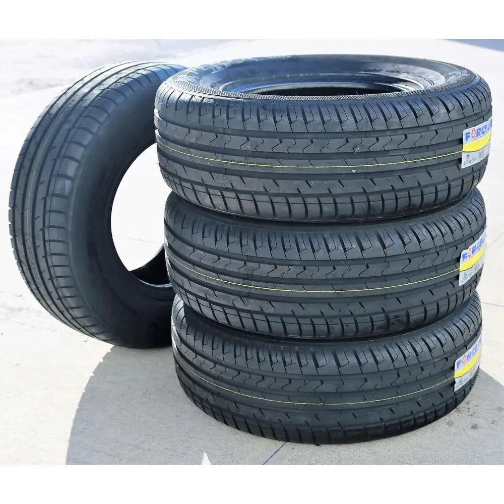 Four black car tires stacked on a light gray concrete surface, with one tire leaning against the stack on the left. Small product labels are visible on the sidewalls.