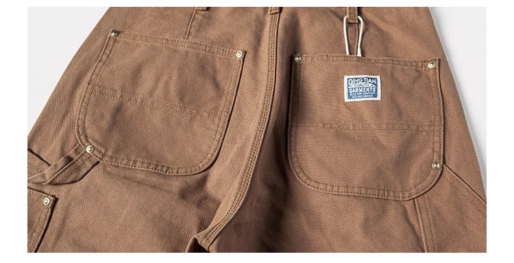 Close-up of brown canvas utility pants showing the back pocket area with a small blue and white brand patch on the right pocket.