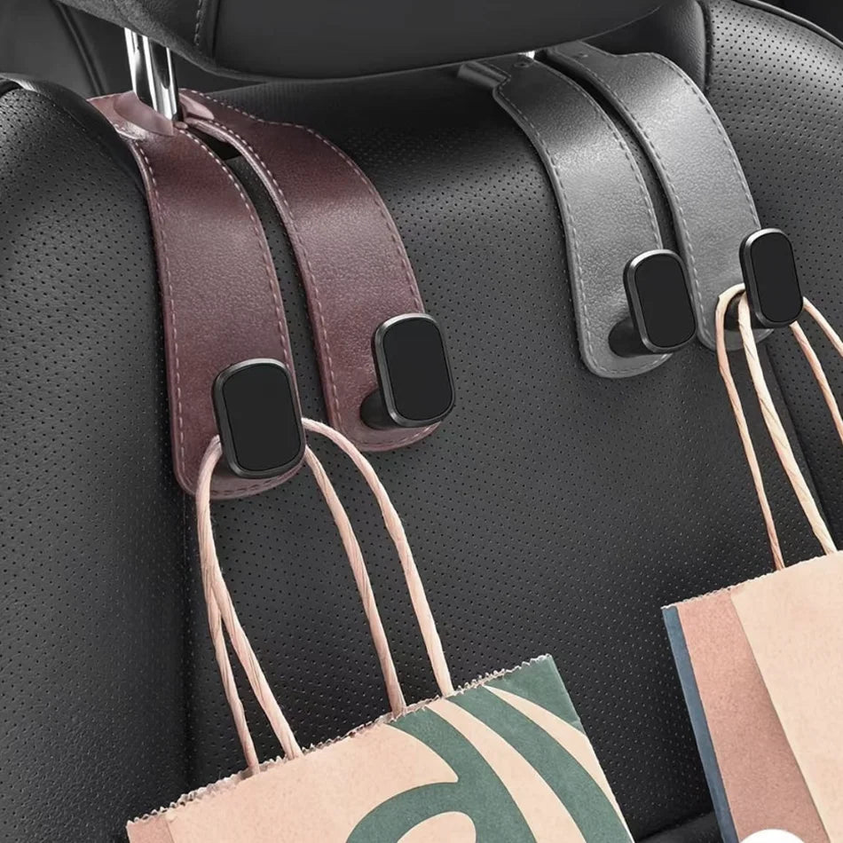 Two car seat belt clip hooks, one in dark brown and one in dark gray, hanging from a black perforated car seat. Shopping bags are draped over the side of the seat to demonstrate how the clips hold the seat belt.